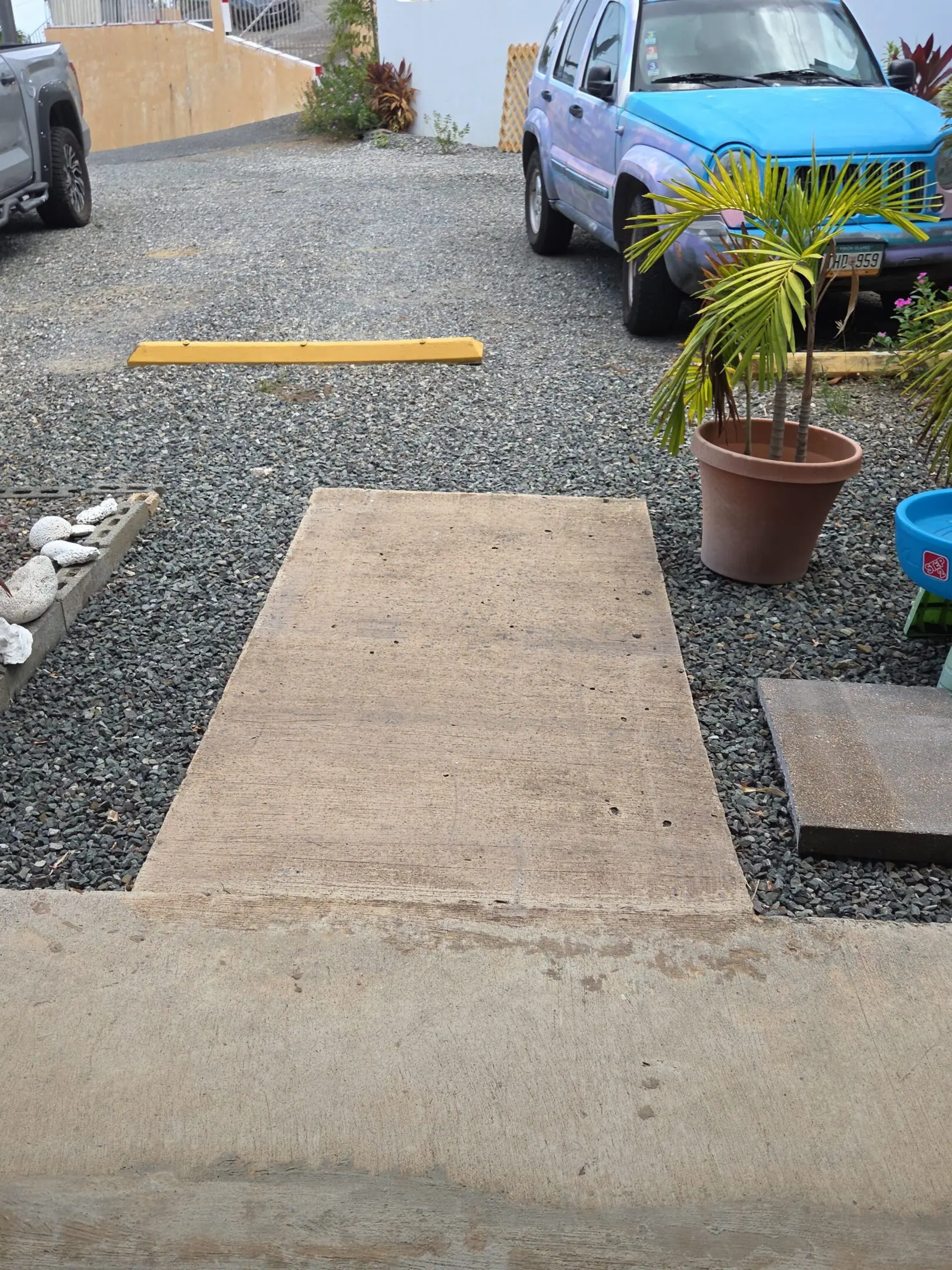 Concrete walkway to gravel parking and blue car