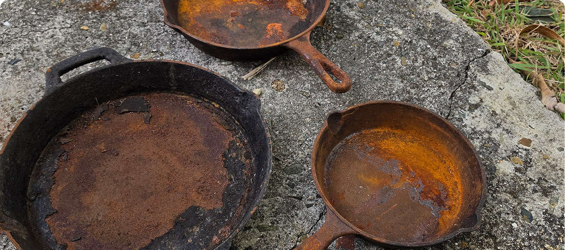 Three rusty cast-iron skillets on concrete